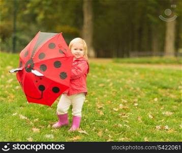 Happy baby playing with red umbrella outdoors