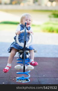 Happy baby swinging on horse on playground