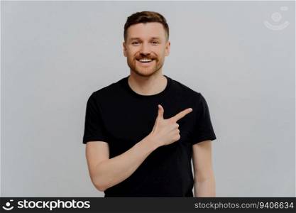 Happy bearded man in black shirt, pointing up, positive expression, promotion concept.