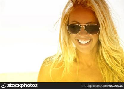 Happy beautiful and sexy young blond woman laughing at the beach in aviator sunglasses