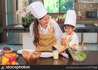 Happy beautiful Asian woman and cute little boy with eyeglasses prepare to cooking in kitchen at home. People and Family concept. Homemade food and ingredients concept. Two Thai people lifestyles