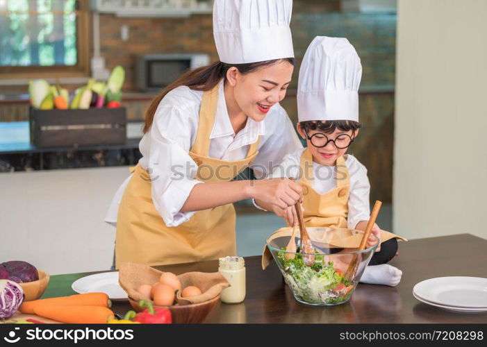 Happy beautiful Asian woman and cute little boy with eyeglasses prepare to cooking in kitchen at home. People lifestyles and Family. Homemade food and ingredients concept. Two Thai people life