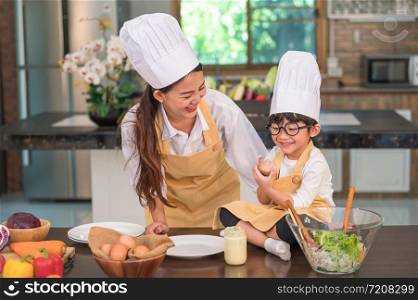 Happy beautiful Asian woman and cute little boy with eyeglasses prepare to cooking in kitchen at home funny. People lifestyles and Family. Homemade food and ingredients concept. Two Thai people life