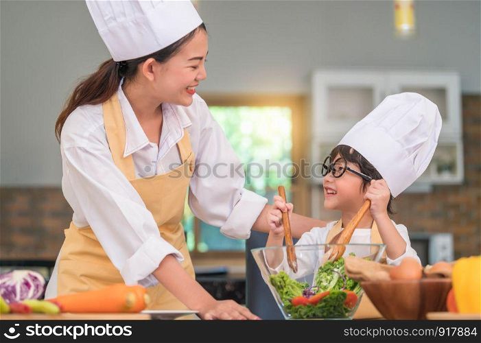 Happy beautiful Asian woman and cute little boy with eyeglasses prepare to cooking in kitchen at home. People lifestyles and Family. Homemade food and ingredients concept. Two Thai people life