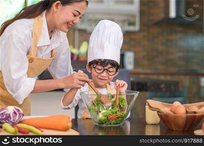 Happy beautiful Asian woman and cute little boy with eyeglasses prepare to cooking in kitchen at home. People lifestyles and Family. Homemade food and ingredients concept. Two Thai people life