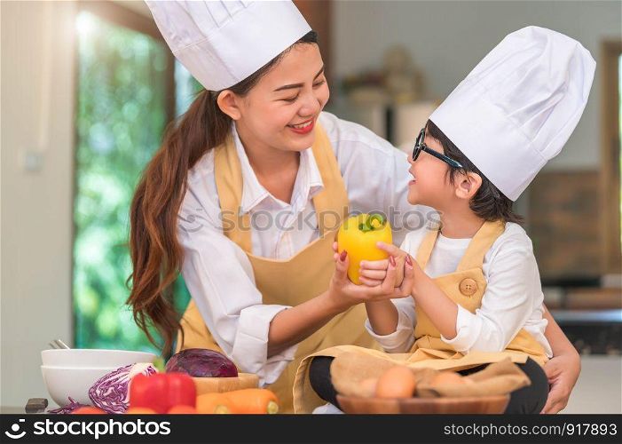 Happy beautiful Asian woman and cute little boy with eyeglasses prepare to cooking in kitchen at home. People lifestyles and Family. Homemade food and ingredients concept. Two Thai looking each other