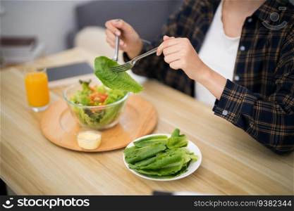 Happy beautiful Asian woman eating healthy food with vegan
salad in the kitchen at home.
