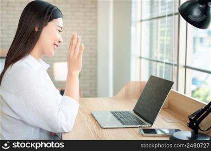 Happy beautiful asian woman working on a laptop and video conference with a colleague at home office sitting at table. Happy female professional freelancer online using notebook pc concept.