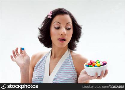 Happy beautiful candy girl with a bowl of colorful bubblegum candy balls licking her lip, isolated