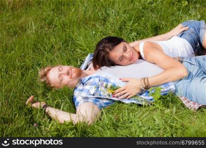 Happy beautiful couple in love lying on the green grass meadow