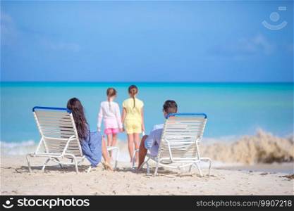Happy beautiful family of four on the beach. Parents relaxing on sunbed and kids having fun on the seashore. Happy beautiful family of four on the beach.