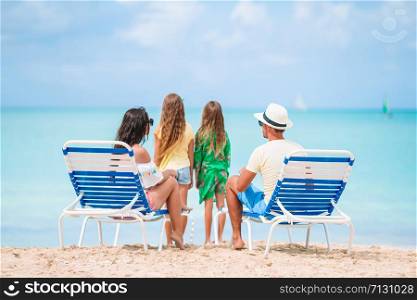 Happy beautiful family on the beach. Back view of parents and kids on the chaise-lounge. Happy family on a beach during summer vacation