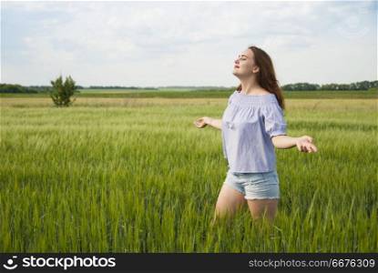 Happy beautiful girl in a field stands with arms outstretched.. Happy beautiful girl in a field enjoying nature.