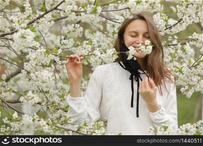 happy beautiful girl took off her medical mask to breathe in the smell of flowers. A girl in a mask stands in blossoms. the end of quarantine.. happy beautiful girl took off her medical mask to breathe in the smell of flowers. A girl in a mask stands in blossoms. the end of quarantine