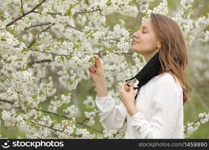 happy beautiful girl took off her medical mask to breathe in the smell of flowers. A girl in a mask stands in blossoms. the end of quarantine.. happy beautiful girl took off her medical mask to breathe in the smell of flowers. A girl in a mask stands in blossoms. the end of quarantine