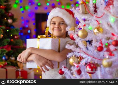 Happy beautiful girl with a gift at a white Christmas tree