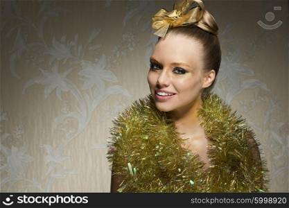 happy beautiful girl with freckles posing with shiny artistic christmas make-up, sparkle tinsel around neck and golden ribbon on hair-style. Smiling and looking in camera