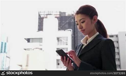 Happy beautiful Japanese female manager speaking on cell phone. Asian businesswoman, confident girl, busy woman at work, talking with smartphone, mobile telephone near office building during break