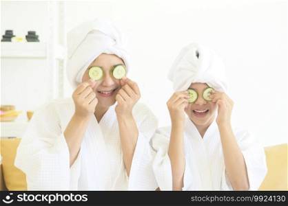 Happy beautiful mom and daughter in white bathrobe applying face mask in bedroom, Family and Beauty Concept. 