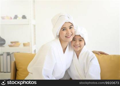 Happy beautiful mom and daughter in white bathrobe applying moisturizing cream on face at home, skin care and treatment concept  