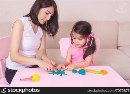 Happy beautiful mother and cute girl playing together with playdough while sitting on table. . Mother and Cute girl playing together with playdough