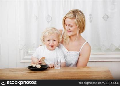 Happy beautiful mother with blond little boy eating bread