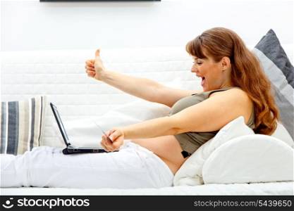 Happy beautiful pregnant female using credit card to shop from the internet&#xA;