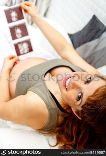 Happy beautiful pregnant woman relaxing on sofa at home and holding echo in hands. &#xA;