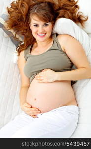 Happy beautiful pregnant woman relaxing on sofa at home and holding her belly.&#xA;