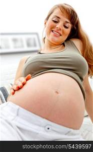 Happy beautiful pregnant woman sitting on sofa at home and holding her belly. Close-up.&#xA;