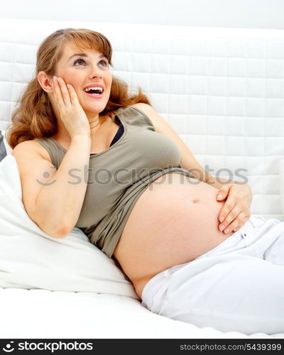 Happy beautiful pregnant woman sitting on sofa at home and holding her belly&#xA;