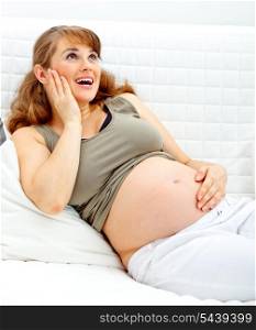 Happy beautiful pregnant woman sitting on sofa at home and holding her belly&#xA;
