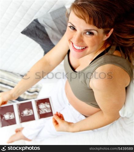 Happy beautiful pregnant woman sitting on sofa at home with echo in hands. &#xA;