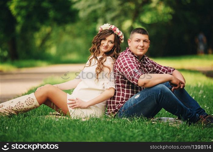 Happy beautiful pregnant woman with his husband sitting on the grass outdoors in the park on summer day. pregnant woman expecting a baby. Future mom and dad, family. mother&rsquo;s, father&rsquo;s day.. Happy beautiful pregnant woman with his husband sitting on the grass outdoors in the park on summer day. pregnant woman expecting a baby. Future mom and dad, family. mother&rsquo;s, father&rsquo;s day