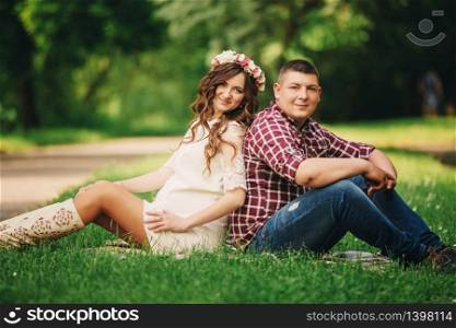 Happy beautiful pregnant woman with his husband sitting on the grass outdoors in the park on summer day. pregnant woman expecting a baby. Future mom and dad, family. mother&rsquo;s, father&rsquo;s day.. Happy beautiful pregnant woman with his husband sitting on the grass outdoors in the park on summer day. pregnant woman expecting a baby. Future mom and dad, family. mother&rsquo;s, father&rsquo;s day