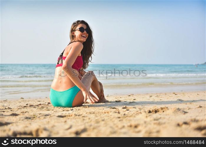 Happy Beautiful woman in a sexy bikini wear sunglasses is sitting on the sand at the beach.