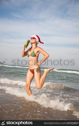 Happy beautiful woman in christmas hat dancing on the beachfront