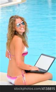 happy beautiful woman is sitting near a swimming pool and using laptop. Laptop screen is cut with clipping path