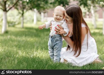 Happy beautiful woman, young mother playing with her adorable baby son, cute little boy, enjoying together a sunny warm day playing on the lawn in a summer garden.. Happy beautiful woman, young mother playing with her adorable baby son, cute little boy, enjoying together a sunny warm day playing on the lawn in a summer garden