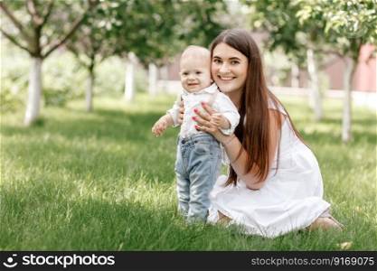 Happy beautiful woman, young mother playing with her adorable baby son, cute little boy, enjoying together a sunny warm day playing on the lawn in a summer garden.. Happy beautiful woman, young mother playing with her adorable baby son, cute little boy, enjoying together a sunny warm day playing on the lawn in a summer garden