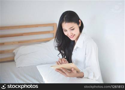 Happy beautiful young asian entrepreneur holding smart tablet sit on sofa or couch in living room at house,smart person working at home person concept.