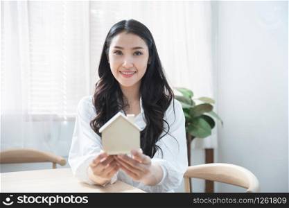 Happy beautiful young asian woman hand holding house sign with smile and relaxation after successful sold real estate property to buyer.