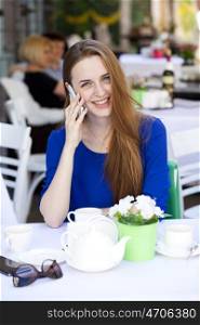 Happy Beautiful young blonde woman calling by phone sitting in a coffee shop