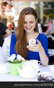 Happy Beautiful young blonde woman reads a message on your smart phone sitting in a coffee shop