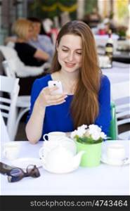 Happy Beautiful young blonde woman reads a message on your smart phone sitting in a coffee shop