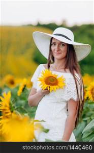Happy beautiful young woman in a white dress and hat in a field of sunflowers enjoys the sunlight. Summer walk on the field of sunflowers of a young girl. selective focus.. Happy beautiful young woman in a white dress and hat in a field of sunflowers enjoys the sunlight. Summer walk on the field of sunflowers of a young girl. selective focus