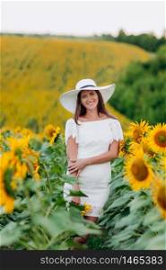 Happy beautiful young woman in a white dress and hat in a field of sunflowers enjoys the sunlight. Summer walk on the field of sunflowers of a young girl. selective focus.. Happy beautiful young woman in a white dress and hat in a field of sunflowers enjoys the sunlight. Summer walk on the field of sunflowers of a young girl. selective focus