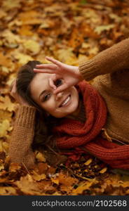 Happy beautiful young woman lying on gold autumn maple leaves enjoy warm weather. Outdoor portrait. Happy beautiful woman lying on autumn leaves
