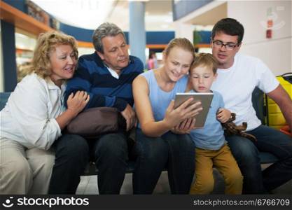 Happy big family at the airport. Child, parents and grandparents watching something on tablet computer to fill in time while waiting in the lounge