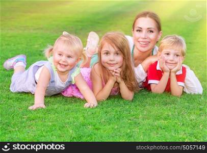 Happy big family having fun outdoors, young mother with three cute kids lying down on fresh green field, love and togetherness concept